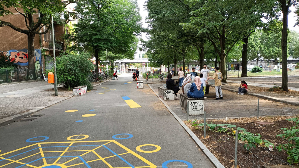 In der Luisenstadt in Berlin-Kreuzberg ist ein Kiezblock geplant. Wo vor zwei Jahren noch Autos abgestellt wurden, verweilen nun Menschen. Ein Blumenbeet lässt Regenwasser absickern und hat einen kühlenden Effekt.